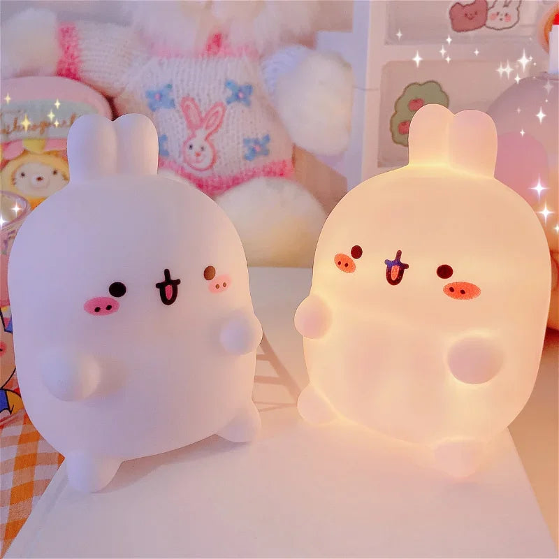 Two cute, cartoonish night lights with animal ears on a soft surface.