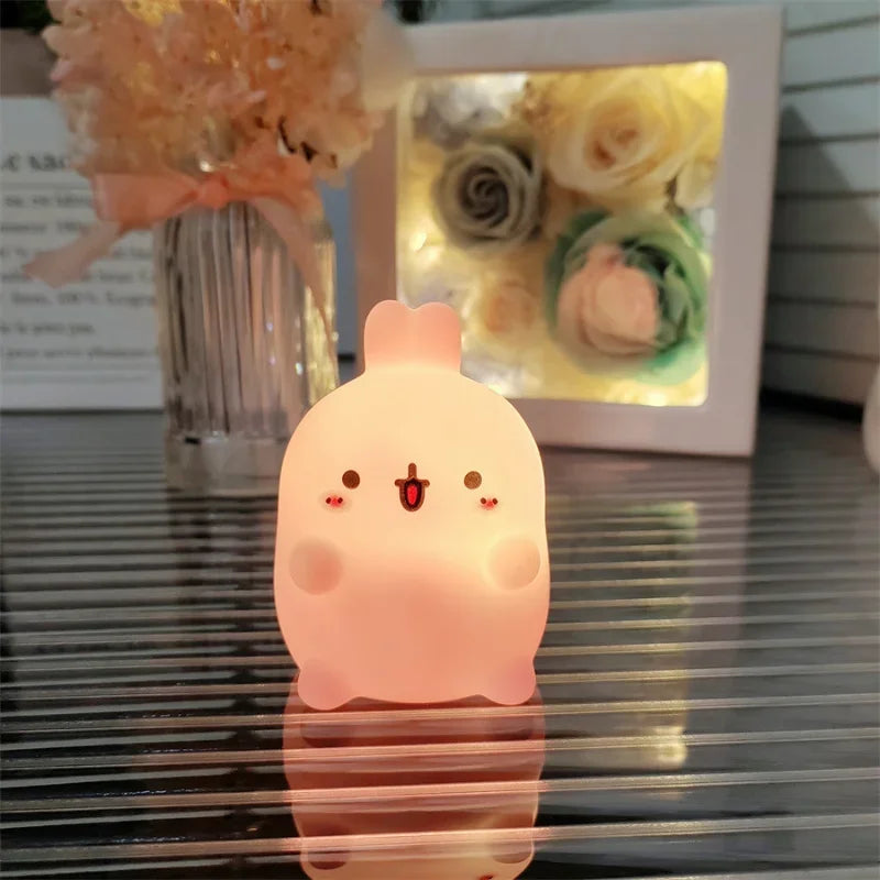 Cute pink cartoon-style night light on a reflective surface with flowers in the background