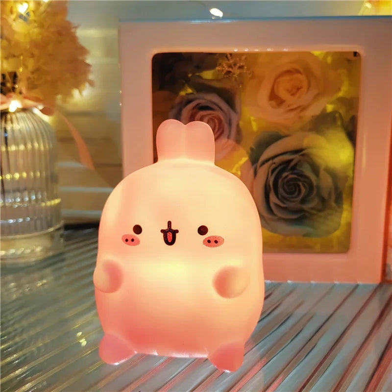 Cute pink cartoon-style lamp on a reflective surface with a floral arrangement in the background.